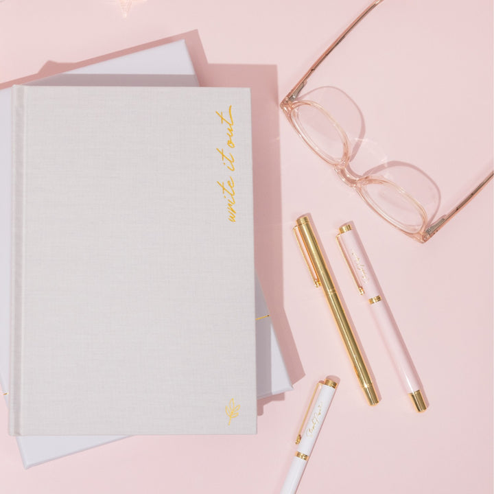 A desk covered in premium ballpoint pens in white metal, pink metal and gold metal.