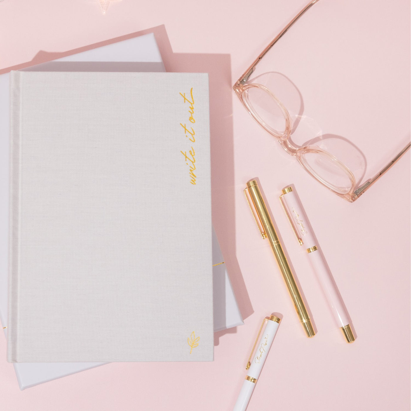 A desk covered in premium ballpoint pens in white metal, pink metal and gold metal.