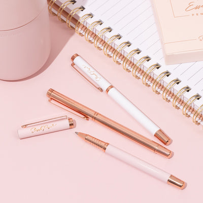 Three Premium metal ballpoint pens in Rose Gold and Pink lie on a desk
