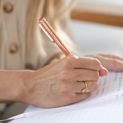 A hand holds a Rose Gold ballpoint pen