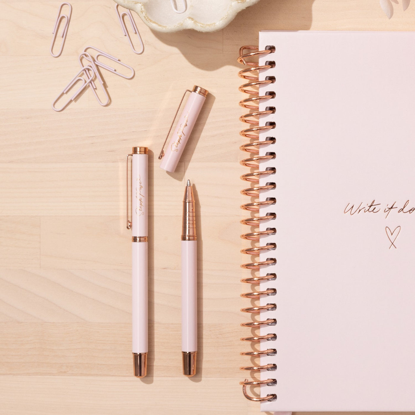 Three Premium metal ballpoint pens in Rose Gold and Pink lie on a desk