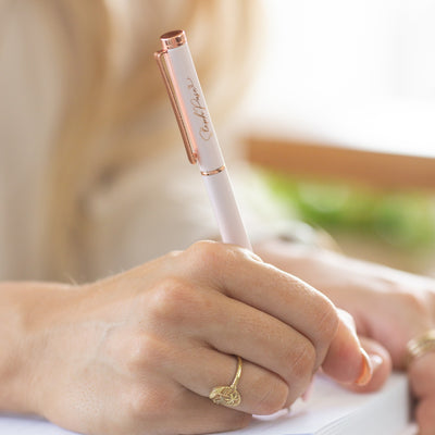 A hand holds a pink and rose gold ballpoint metal pen