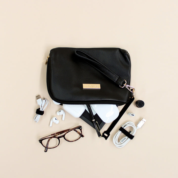 Black faux leather cable organiser bag with zip, removable strap, tech loops and multiple storage pockets. Filled with air pods, mouse, charging cables and glasses.