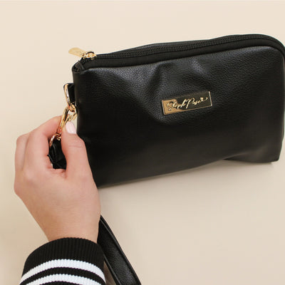 Hand removing wrist strap from a Black faux leather cable organiser bag with zip, velcro tech loops and multiple storage pockets.