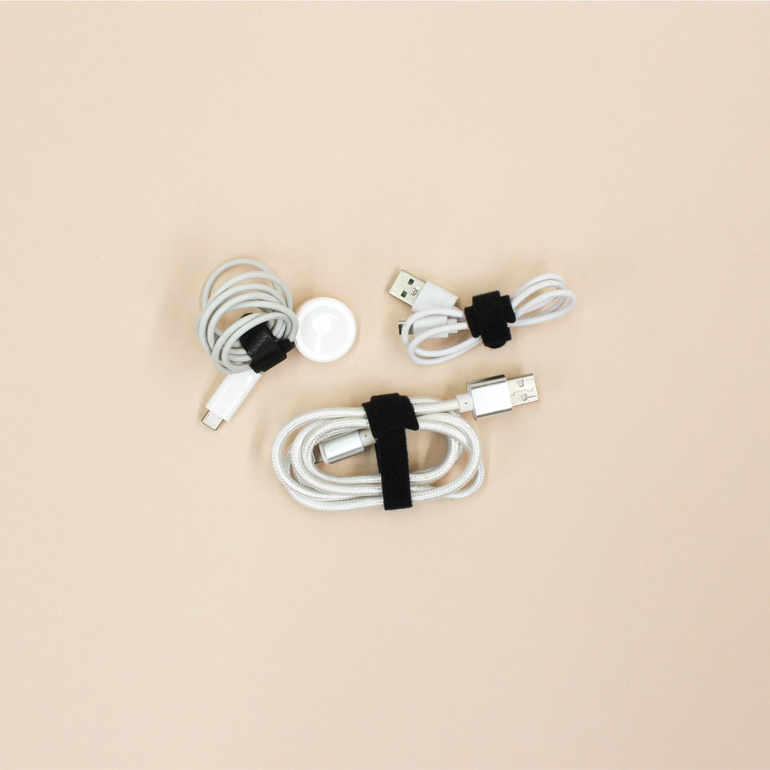 Set of white charging cables with black velcro loop ties on a beige background